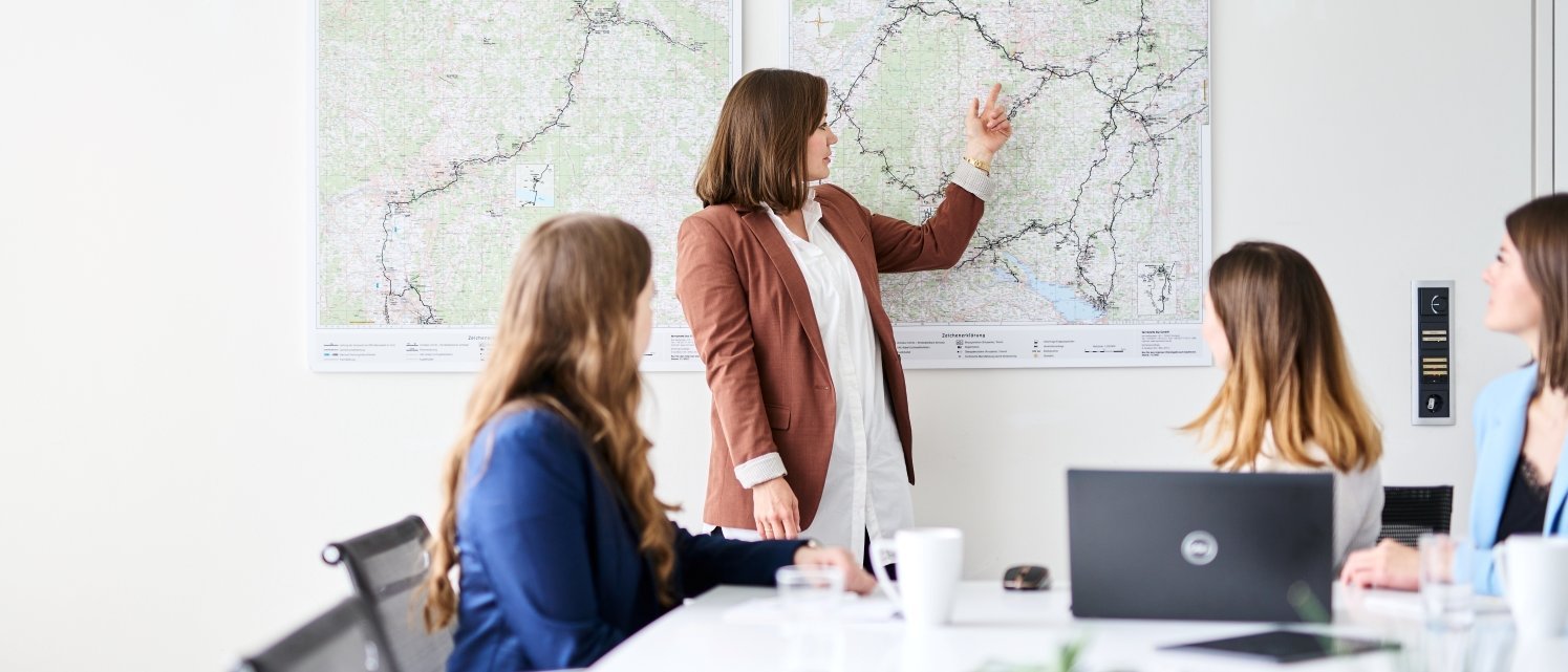 Drei Mitarbeiterinnen von terranets&nbsp;bw im Workshop, eine Person zeigt den anderen Personen etwas auf einer Netzkarte, ein Laptop und eine Tasse auf dem Tisch